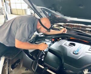 The BMW Guy mechanic looking under the car hood.