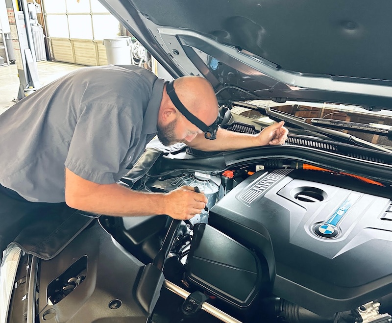 The BMW Guy mechanic looking under the car hood.